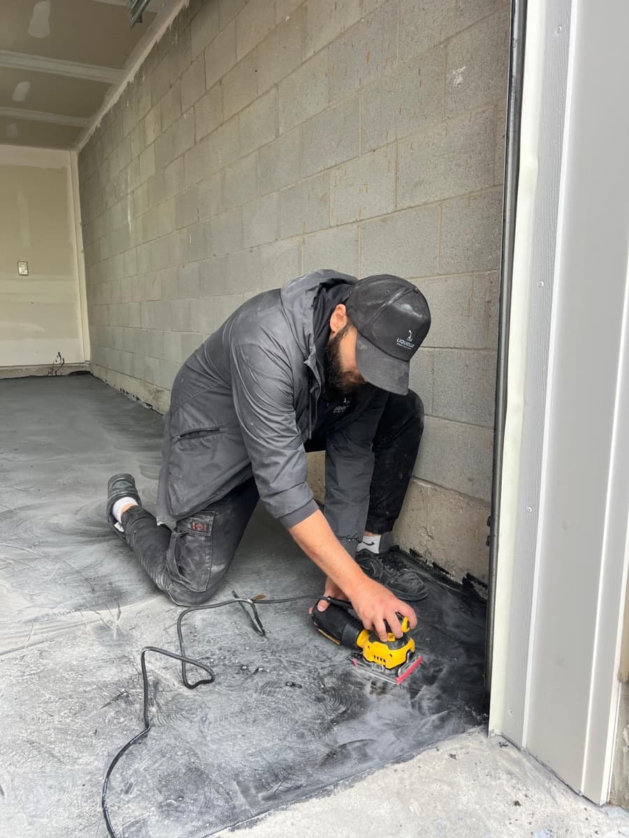 An installer hand-sanding the garage floor edge before coating
