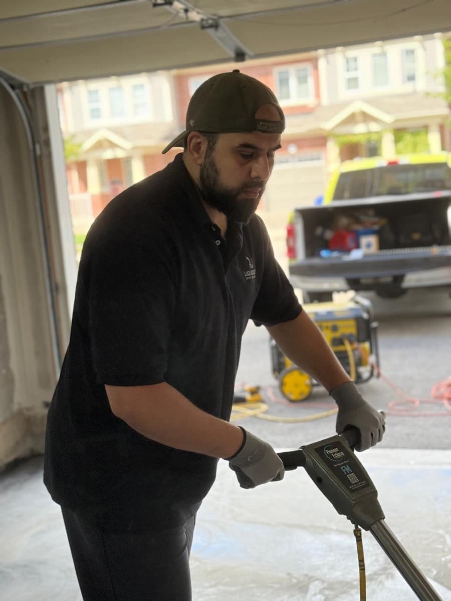 A LiquidLux installer in branded uniform running a floor grinder in a customer's driveway